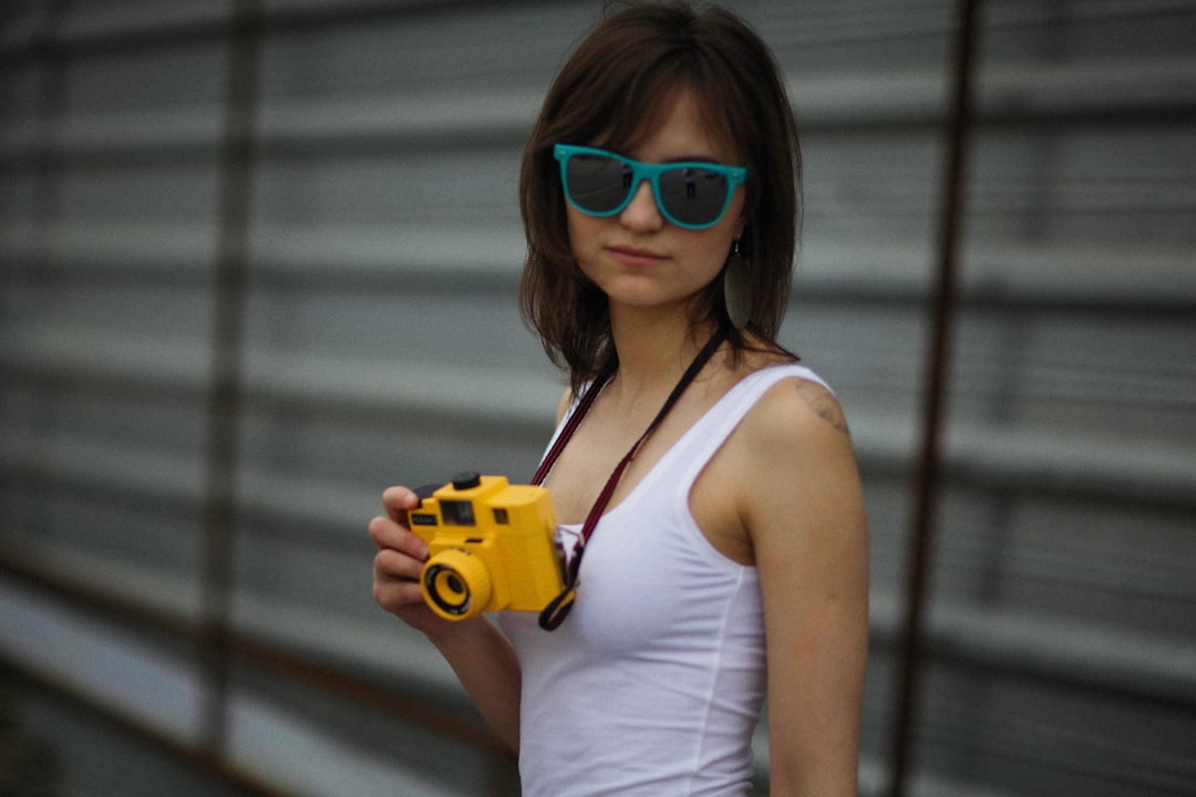 a-woman-wearing-sunglasses-holding-a-yellow-camera-jp7-6zswqv4